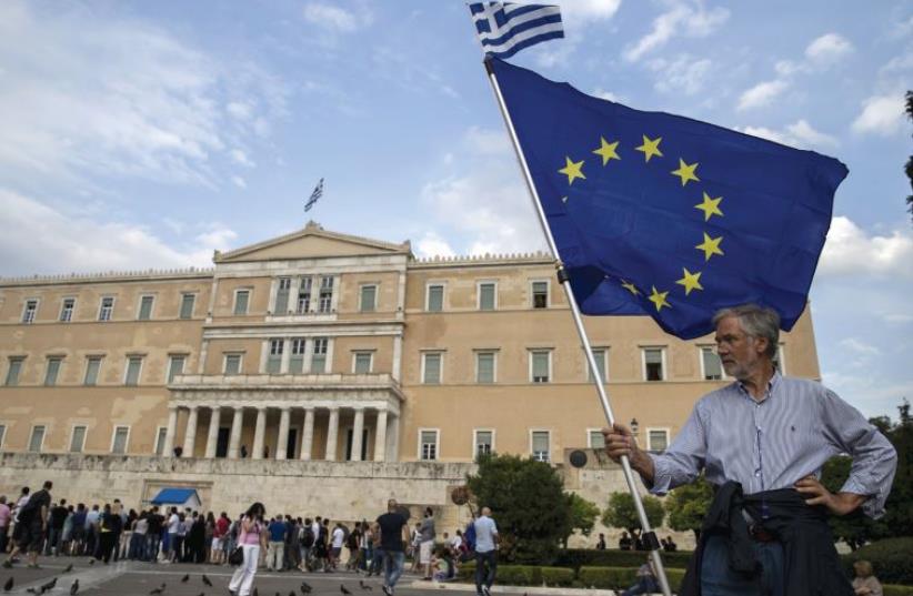 A pro-euro protester holds a European Union flag with a Greek national flag on top during a rally in front of the parliament building in Athens (photo credit: REUTERS)