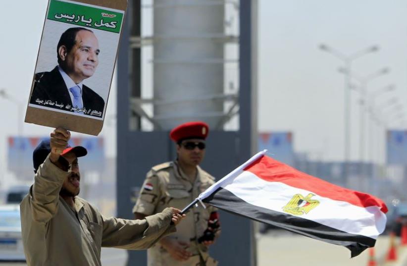 A man carrying a portrait of Egyptian President Abdel Fattah al-Sisi and an Egyptian flag stands next to a soldier during the funeral of Egyptian public prosecutor Hisham Barakat (photo credit: REUTERS)