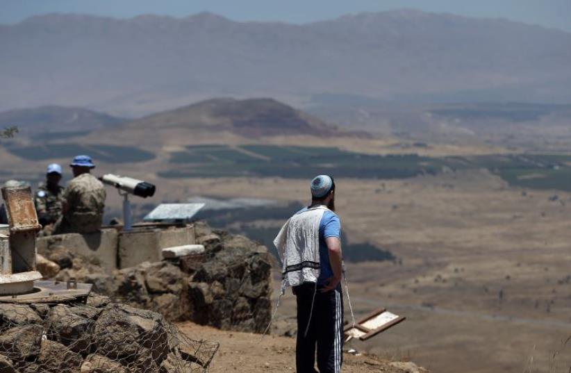 A Jewish man observes Syria from an Israeli army post guarded by UN peacekeepers (L) on Mount Bental in the Golan Heights (photo credit: THOMAS COEX / AFP)