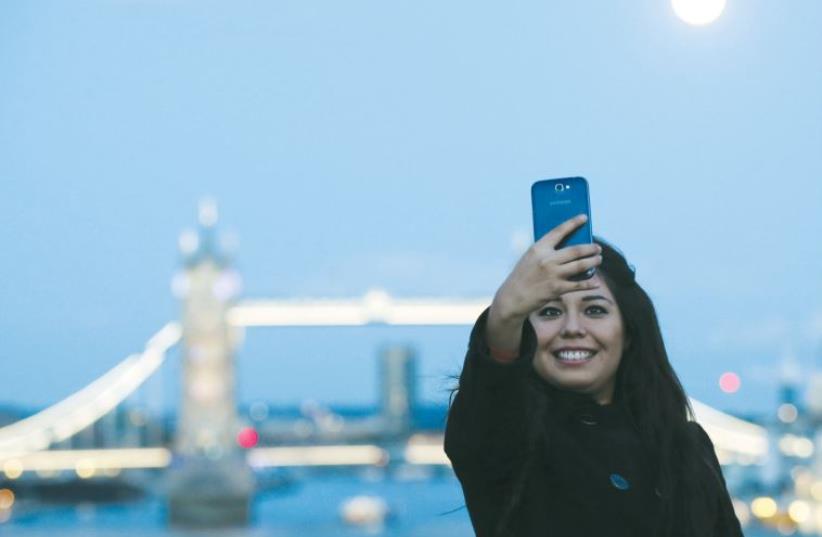 A woman takes a selfie with the London Bridge in the background (photo credit: ILLUSTRATIVE: REUTERS)
