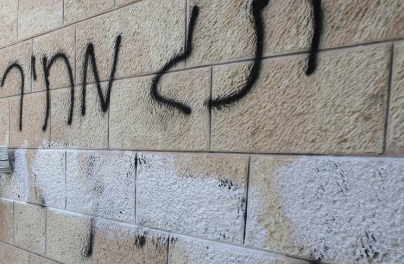 A municipal worker paints over ‘price tag’ graffiti daubed in Hebrew on a wall of the Romanian Orthodox Church in Jerusalem, May 9, 2014. (photo credit: AMMAR AWAD / REUTERS)