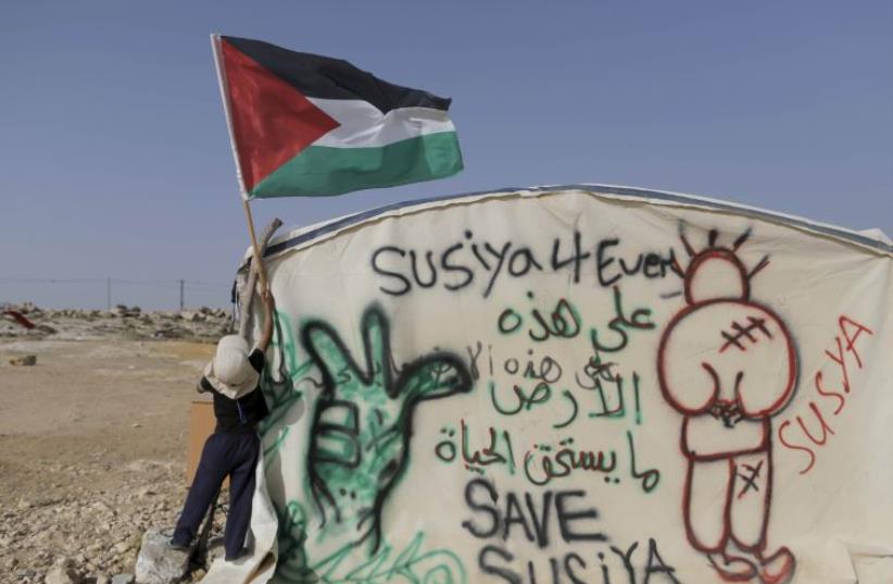 A Palestinian boy places a Palestinian flag on a tent in the West Bank village of Sussiya (photo credit: REUTERS)
