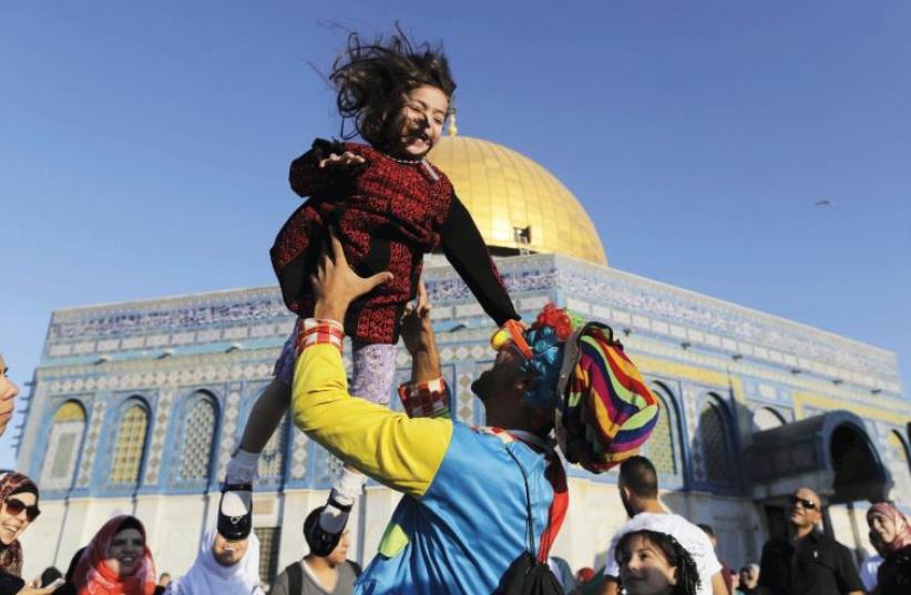 A MAN DRESSED as a clown plays with a girl on Friday, Id al-Fitr, near the Dome of the Rock on Jerusalem’s Temple Mount (photo credit: REUTERS)