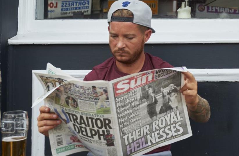 A man reads The Sun showing photo of the young Queen Elizabeth II giving Nazi salute.  (photo credit: NIKLAS HALLE'N / AFP)