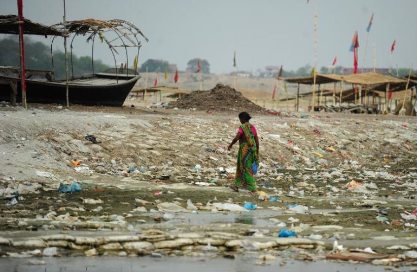 An Indian woman walks amogst plastic bags and garbage strewn on the banks of the River Ganges at Sangam (photo credit: SANJAY KANOJIA / AFP)