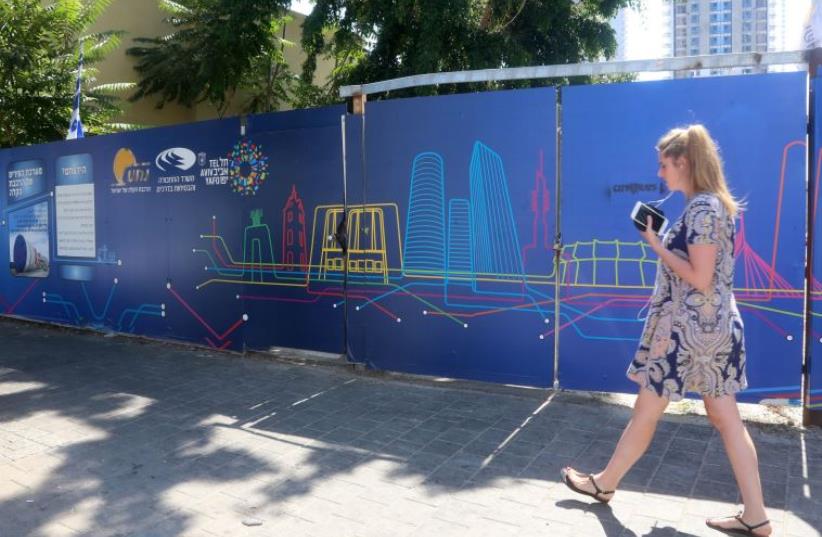 A woman walks in front of a sign advertising the Tel Aviv Light Rail  (photo credit: MARC ISRAEL SELLEM/THE JERUSALEM POST)