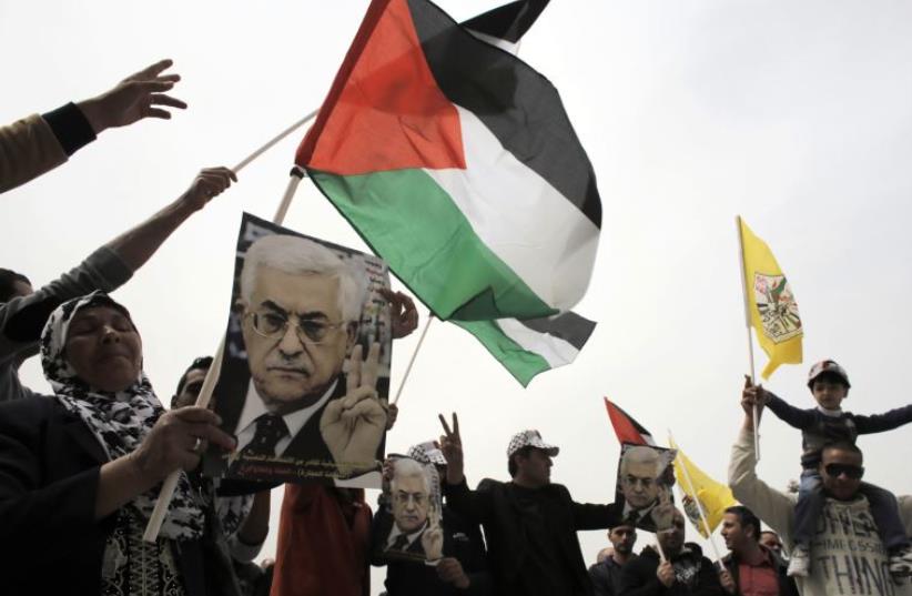 Palestinians hold flags and posters depicting PA Mahmoud Abbas during a rally in Bethlehem  (photo credit: REUTERS)