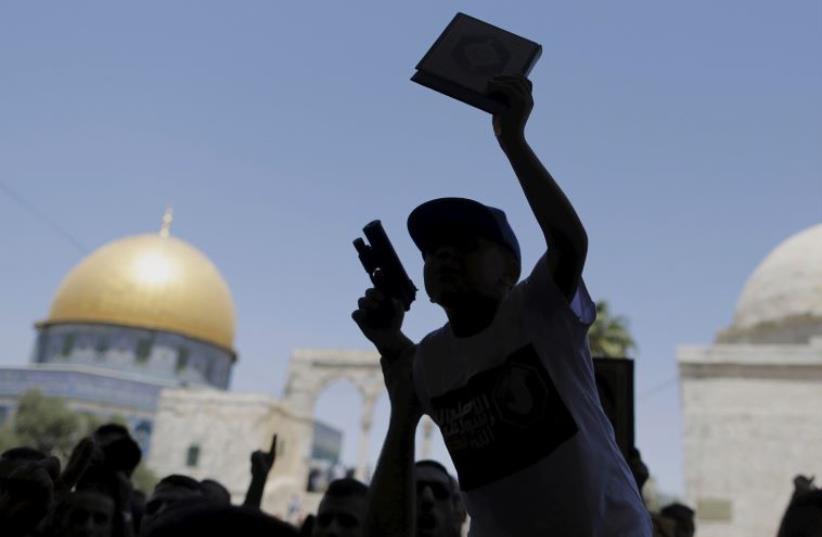 A Palestinian youth is silhouetted as he holds a toy gun and a Koran during a protest after Friday prayers on Temple Mount in Jerusalem's Old City (photo credit: REUTERS)