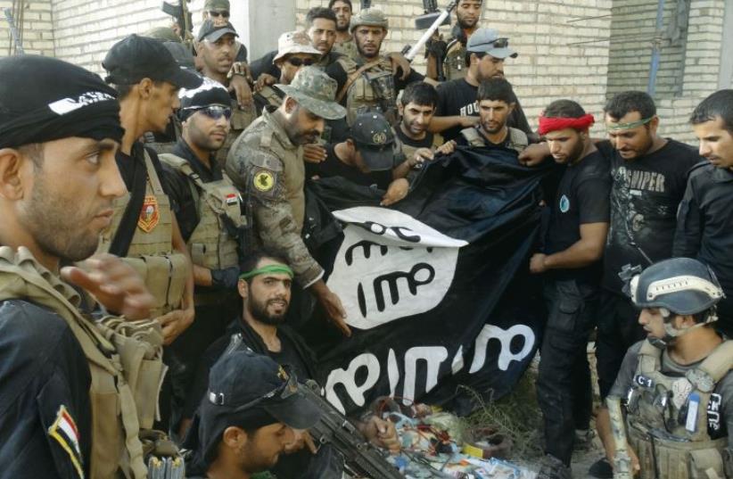 Iraqi security forces hold an Islamist State flag which they pulled down at the University of Anbar, in the western city of Ramadi on Sunday. (photo credit: REUTERS)