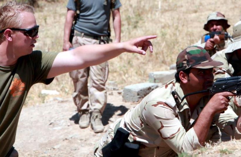 An officer from the Western coalition forces gives advice to Kurdish Peshmerga forces during a training session on how to defend the front lines against ISIS in Daquq district, northern Iraq, June 15 (photo credit: AZAD LASHKARI / REUTERS)