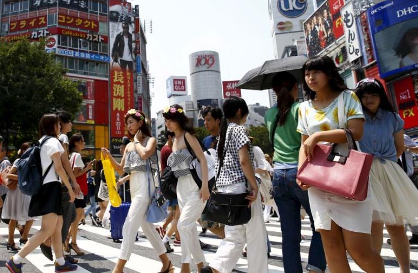 People cross a junction in front of advertising billboards in the Shibuya shopping district in Tokyo (photo credit: REUTERS)