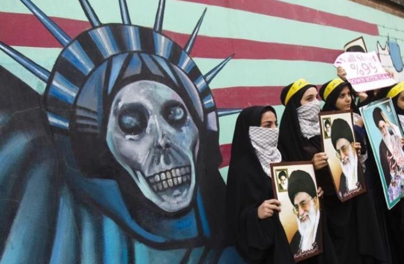 Iranian students hold pictures of Iran's Supreme Leader Ayatollah Ali Khamenei in front of an anti-US mural, painted on the wall of the former US Embassy in Tehran (photo credit: REUTERS)