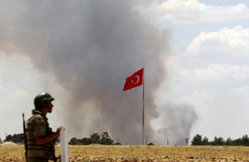 A Turkish soldier stands guard while smoke rises in the Syrian town of Kobani as it is seen from the Turkish border town of Suruc (photo credit: REUTERS)