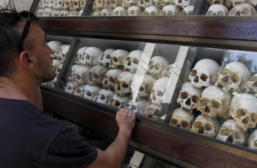 A tourist looks at skulls and bones of more than 8,000 victims of the Khmer Rouge regime displayed at Choeung Ek, a "Killing Fields" site located on the outskirts of Phnom Penh July 2, 2015.  (photo credit: REUTERS)