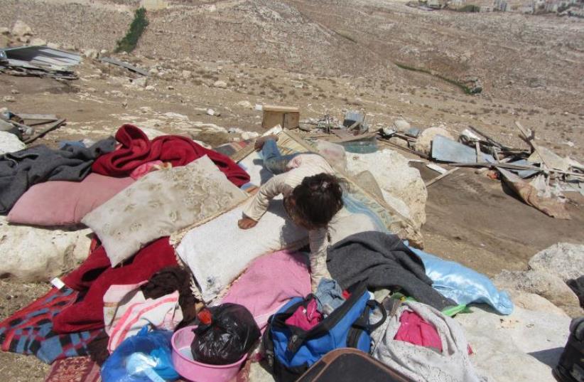 A girl climbs on top of belongings that were in illegal structures in the Beduin Al-Khdeirat community (photo credit: B'TSELEM)