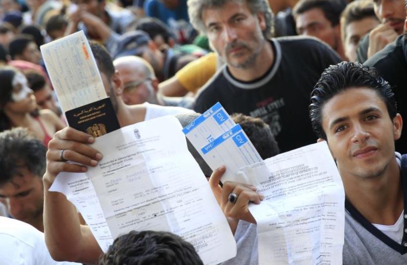 Refugees raise their documents and railways tickets outside the Keleti station in Budapest, Hungary  (photo credit: REUTERS)