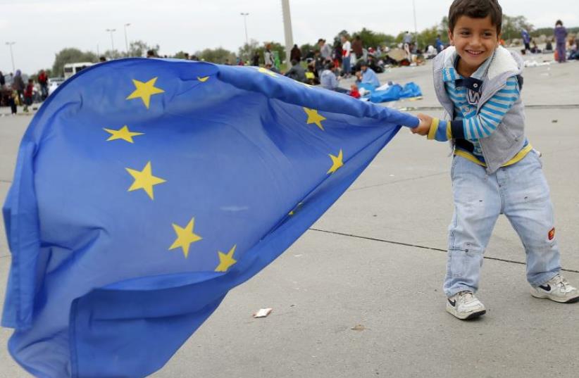 A young migrant child plays with a European Union flag after crossing the Austrian border in Nickelsdorf (photo credit: REUTERS)