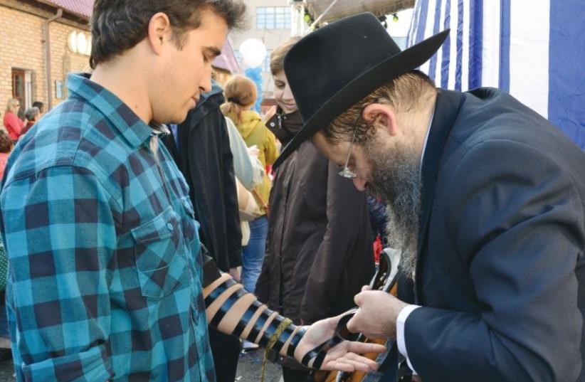 A rabbi wraps tefillin on a young man during the Jewish festival in Kazan (photo credit: LAURA KELLY)