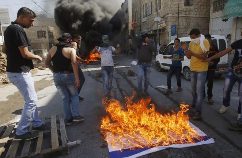 Palestinians in Hebron burn an Israeli flag while clashing with IDF troops (photo credit: REUTERS)