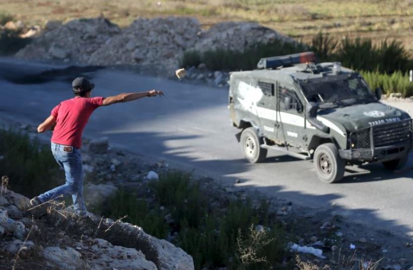 A Palestinian throws a stone at a Border Police vehicle during a protest near Ramallah (photo credit: REUTERS)