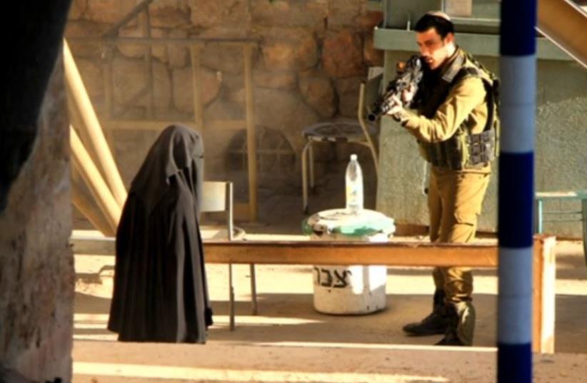 An IDF soldier aiming at Hadeel al-Hashlamun after she refused requests to put down her weapon and lunged at soldiers (photo credit: REUTERS)