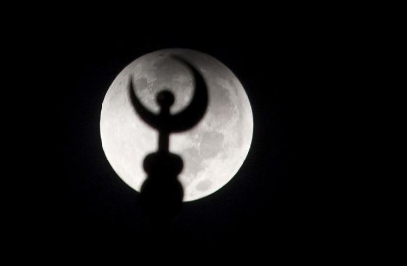 A minaret of a mosque is silhouetted against the moon at the start of a total "supermoon" lunar eclipse in Salhiya, Kuwait City (photo credit: REUTERS)