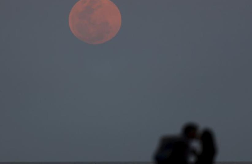 A couple kisses as a supermoon rises in the sky over the Rio de La Plata in Buenos Aires (photo credit: REUTERS)