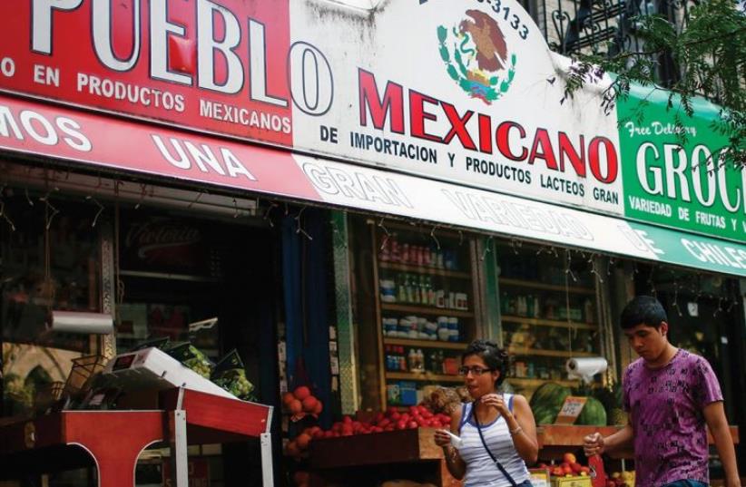PEOPLE PASS by a Mexican grocery store in Harlem, New York. (photo credit: REUTERS)