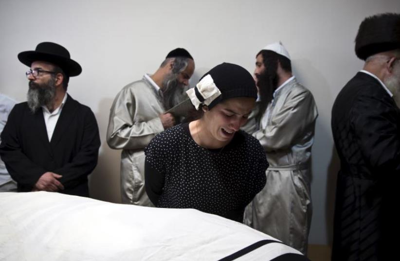 A relative of Aharon Banita mourns next to his covered body before his funeral in Jerusalem (photo credit: REUTERS)