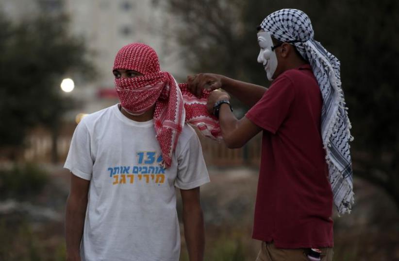 A Palestinian youth helps another put on a scarf during clashes with IDF soldiers close to Bet El, in the West Bank (photo credit: ABBAS MOMANI / AFP)
