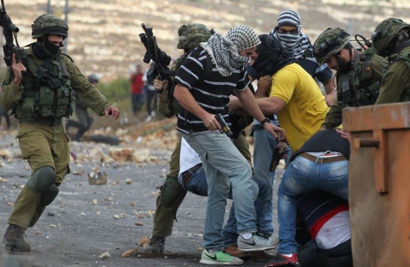 Israeli soldiers and infiltrated members of the Israeli security forces detain a Palestinian stone thrower (R-bottom) during clashes in Beit El, on the outskirts of the West Bank city of Ramallah, on October 7, 2015 (photo credit: ABBAS MOMANI / AFP)