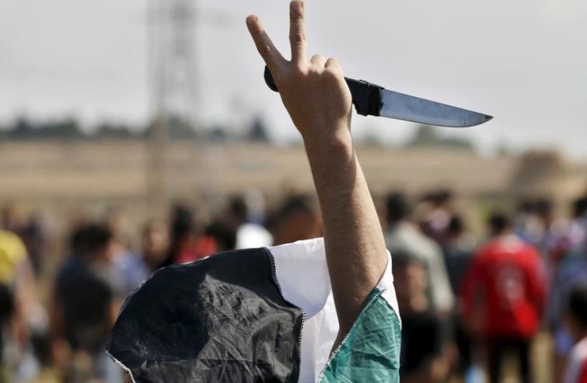 A masked Palestinian protester holds a knife during a protest near the Israeli border fence in northeast Gaza (photo credit: REUTERS)