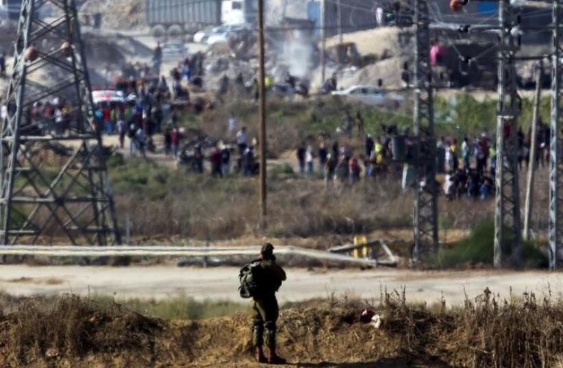 An IDF soldier aims his rifle towards Palestinian protestors during clashes over the border fence between Israel and Gaza, October 11, 2015 (photo credit: REUTERS)