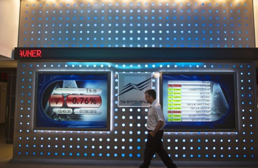 An employee walks past a screen displaying market data at the Tel Aviv Stock Exchange (photo credit: REUTERS)