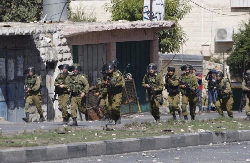 IDF soldiers take up a position during clashes with Palestinian protesters in the West Bank city of Hebron October 13, 2015 (photo credit: REUTERS)