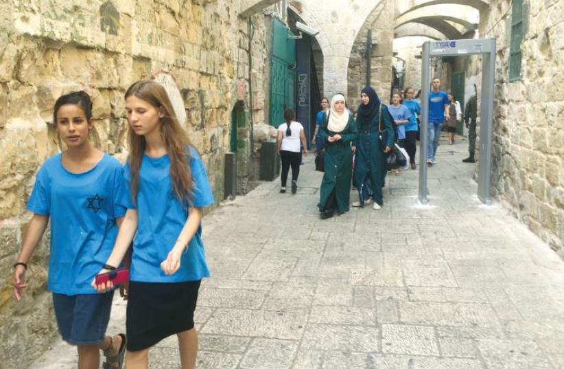 Muslim and Jewish women walk past one of the newly installed metal detectors in the Old City (photo credit: SETH J. FRANTZMAN)