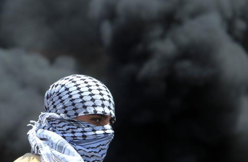 A masked Palestinian protester looks on amid the smoke of burning tires during clashes with Israeli security forces near Nablus (photo credit: AFP PHOTO)