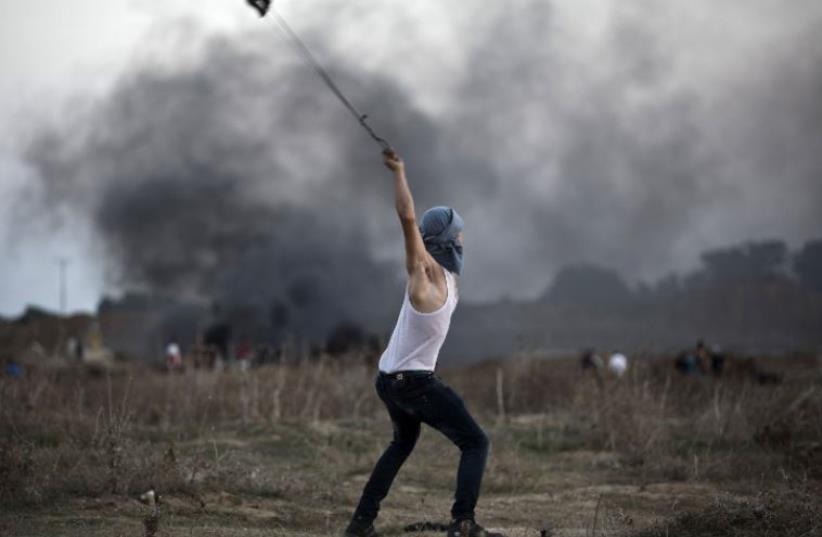 A Palestinian protester uses a slingshot to throw stones towards Israeli soldiers during clashes near the border fence between Israel and the central Gaza Strip east of Bureij (photo credit: AFP PHOTO)