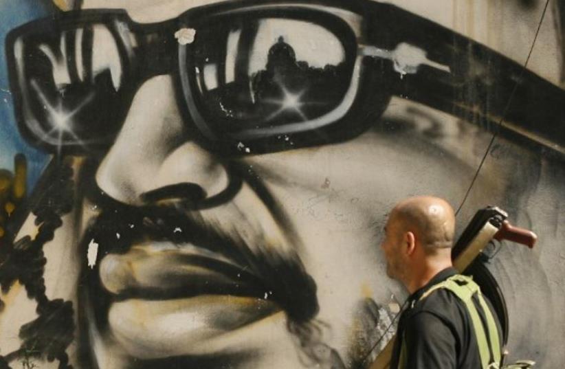 An armed man walks past a graffiti depicting late Palestinian leader Yasser Arafat in Lebanon's southern Palestinian refugee camp of Ain El-Helweh (photo credit: AFP PHOTO)