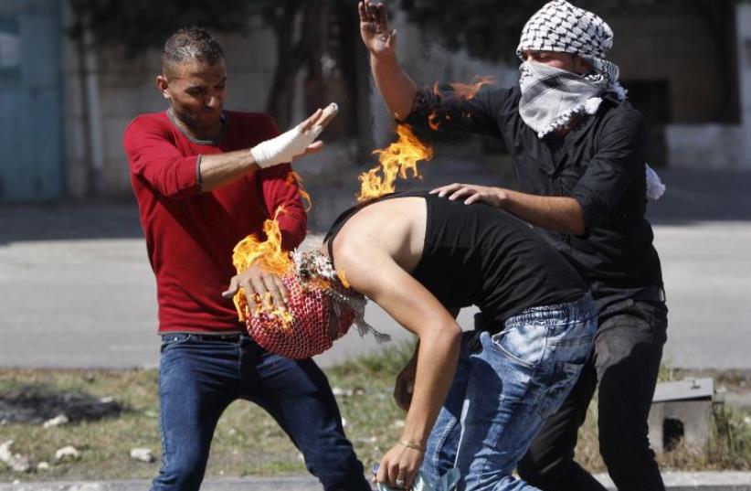 Palestinian protesters put out a fire burning on a compatriot, caused by a Molotov cocktail which he was trying to hurl at Israeli troops in Hebron (photo credit: REUTERS)