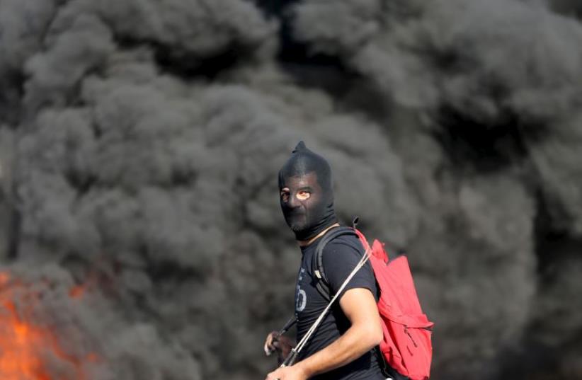 A Palestinian protester takes a position as smoke rises from a fire behind him during clashes with Israeli troops near the Jewish settlement of Beit El (photo credit: REUTERS)