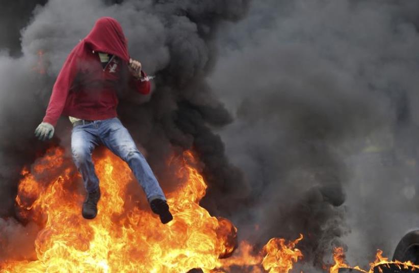 A Palestinian protester jumps over burning tires during clashes with IDF troops near the Jewish settlement of Beit El (photo credit: REUTERS)