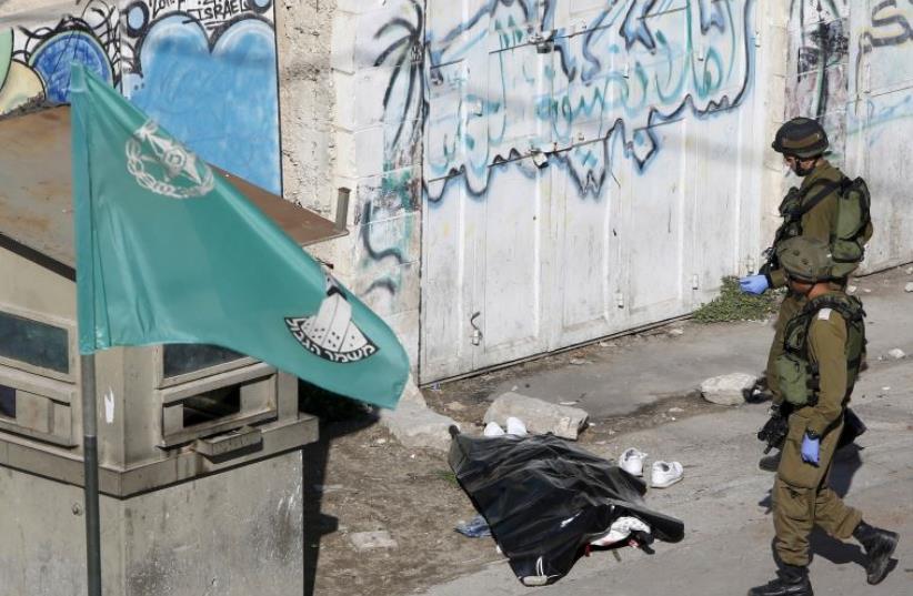 Israeli soldiers stand next to the body of a Palestinian who moments earlier stabbed a soldier in Hebron (photo credit: REUTERS)
