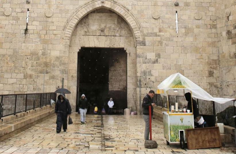 A man buys street food as it rains near Damascus Gate in Jerusalem's Old City (photo credit: REUTERS)