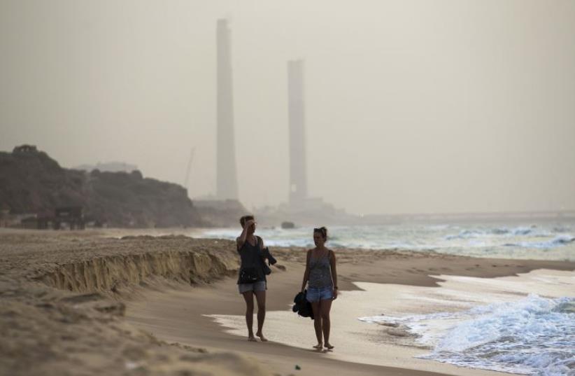 Tourists walk at the shore of the Mediterranean sea in Ashkelon in southern Israel during heavy hazy weather in the region (photo credit: REUTERS)