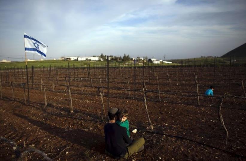 A Jewish man holds his son at a vineyard belonging to Mitzpe Kramim, east of Ramallah in the West Bank (photo credit: REUTERS)