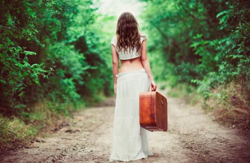 Young woman with suitcase in hand going away by a rural road (photo credit: INGIMAGE)