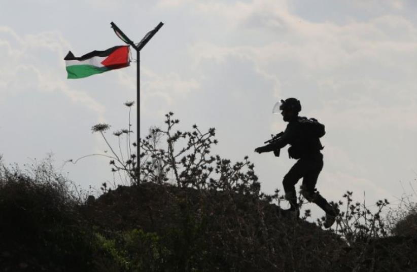 A member of the Israeli security forces runs past a Palestinian flag during clashes with Palestinian stone throwers in the West Bank town of Tul Karm (photo credit: AFP PHOTO)