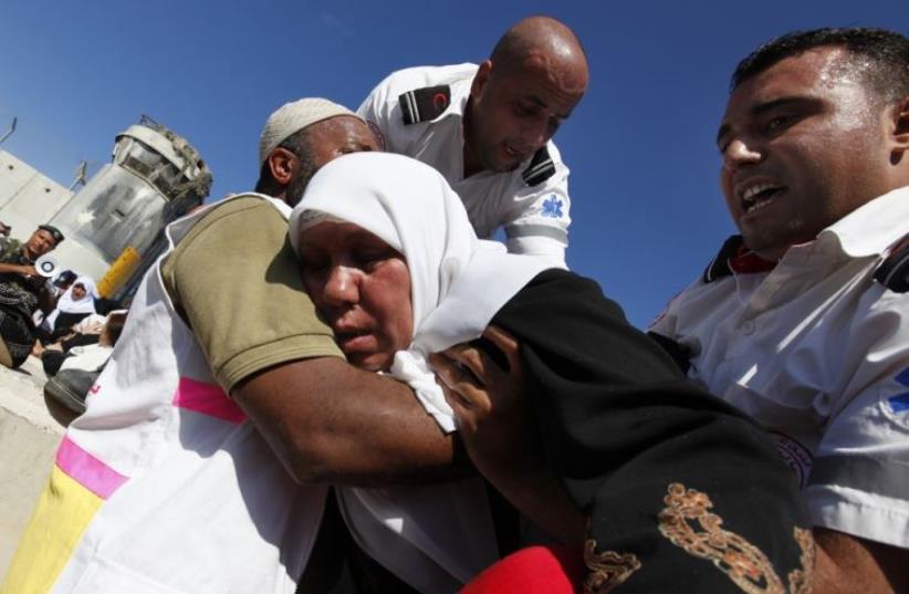 Red Crescent workers help a Palestinian woman after she fainted during a stampede as Palestinian women crowd the Qalandiya checkpoint near the West Bank city of Ramallah (photo credit: REUTERS)