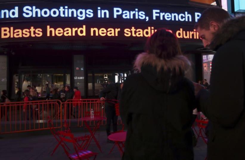 People watch as a news ticker updates people with the news of the shooting attacks in Paris, in Times Square in the Manhattan borough of New York November 13, 2015 (photo credit: REUTERS)